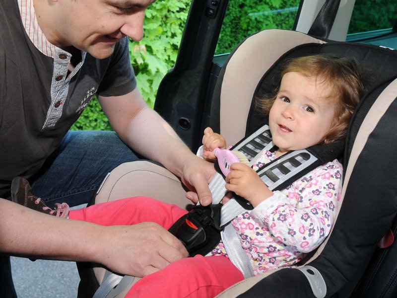 Junger Vater schnallt seine Tochter im Kindersitz an. 
